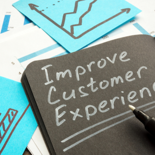 Notebook with the words “Improve Customer Experience” written on it, surrounded by business charts and graphs.